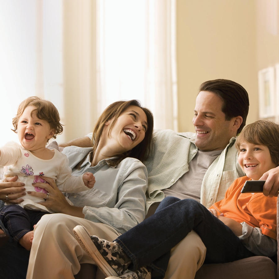 Family of four, mother, father and two child, smiling while sitting on couch