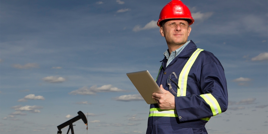 man wearing hardhat holding a tablet with drilling equipment in background