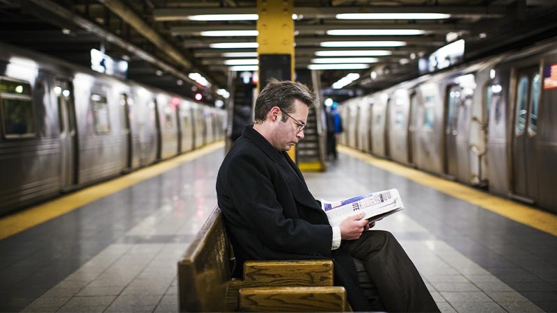 A man in a black suit reading on a bench, waiting for rail electric transport