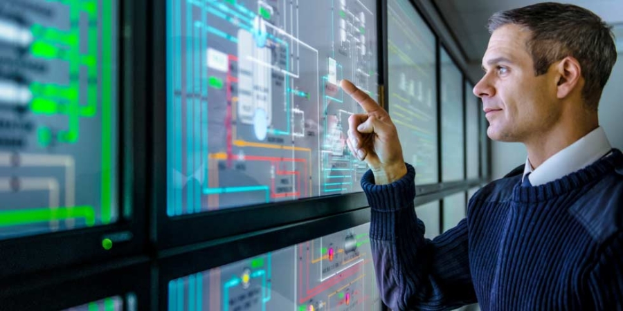 Facilities manager using energy monitoring software on a multiple screen view, industrial energy management.