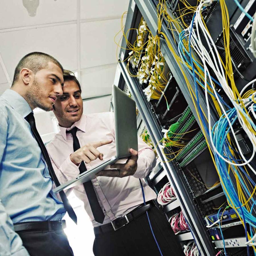 Two men looking at laptop computer in a network data center, energy management software, energy efficiency.