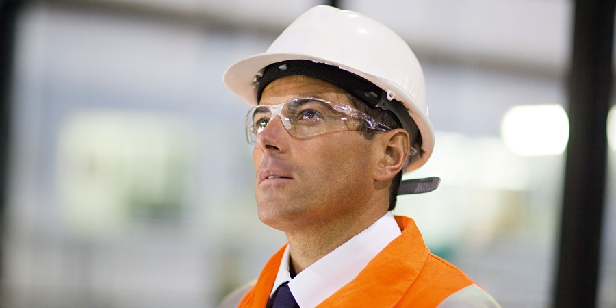 construction worker wearing orange vest and white helmet looking up