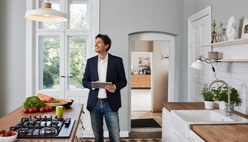 A person in a suit holding a tablet in a kitchen