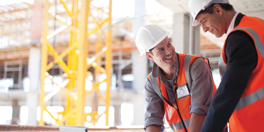 two construction workers in a factory smiling while looking at each other