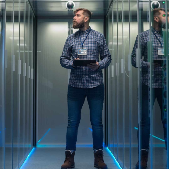 Portrait of adult bearded man and woman standing in corridor of server room in data center smiling at camera