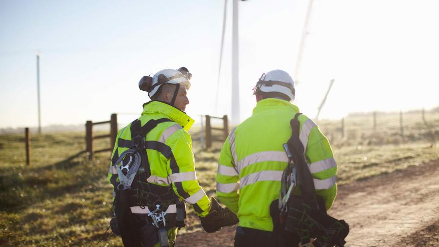 Two engineers at wind farm, walking together.