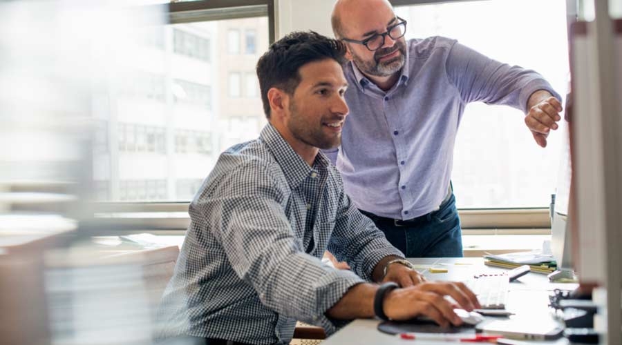 Office life. Two men in an office, using a computer screen.