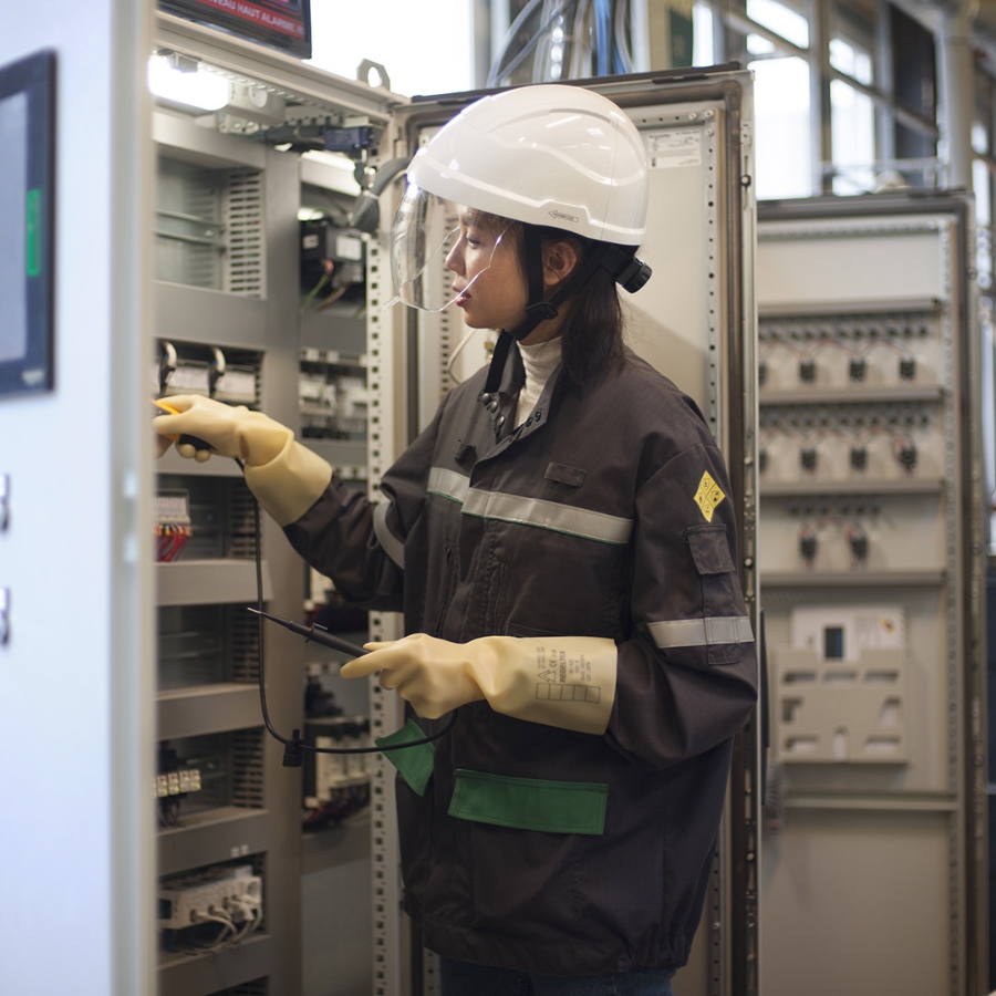 Female employee in safety clothing repairing a control panel inside a factory