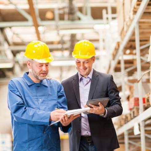 Regardless of equipment age, we have service options that include Maintenance, Remote Management, Spare Parts, Training, Modernization and Consultation; aligned to 5 key phases of the Asset Management Life Cycle. Worker and manager in warehouse.