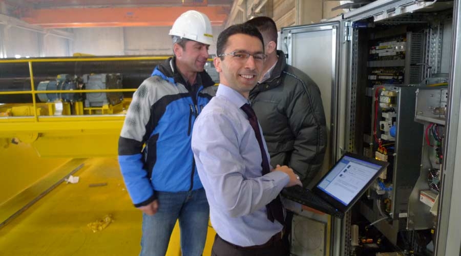 Smiling technician with laptop in front of control panel, industrial automation, facility management software.