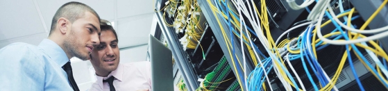 Two men looking at laptop computer in a network data center, energy management software, energy efficiency.