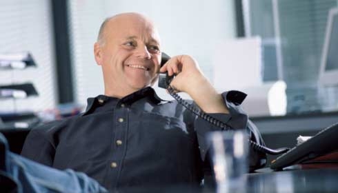 Man at office desk using telephone, smiling