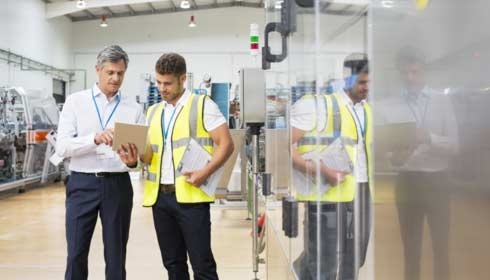 Supervisor and worker using digital tablet in factory