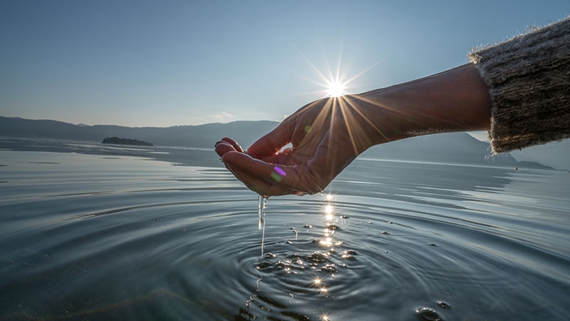 Human hand cupped to catch fresh water from lake. Shot in Italy at the lake Maggiore, beautiful sunset, sunbeam reflections on the water surface. Environment concept idea.