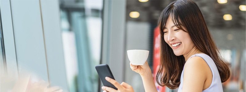 Asian woman using mobile phone and drinking a cup of coffee in modern coffee shop