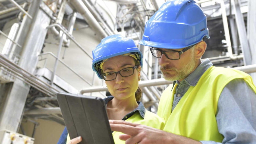 A person and person wearing hard hats looking at a tablet